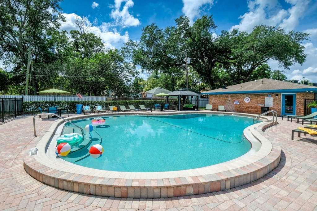 Community pool at Watermarq luxury Apartments Lakeland, FL with tile flooring, inflatable pool toys, and large pool house.