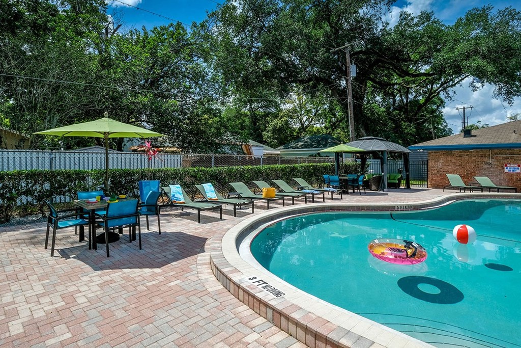 Green lounge chairs and patio tables with umbrellas next to community pool at the Watermark Apartments in Lakeland, Fl.