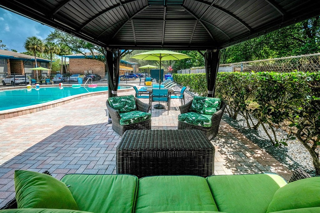 Luxury poolside lounge at the Watermark Apartments in Lakeland, Fl with cushioned wicker patio seating and table under large shade.