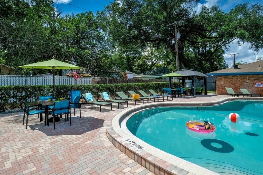 Poolside view of Community pool at Watermark luxury Apartments in Lakeland, FL with green lounge chairs and patio tables with sun umbrellas.