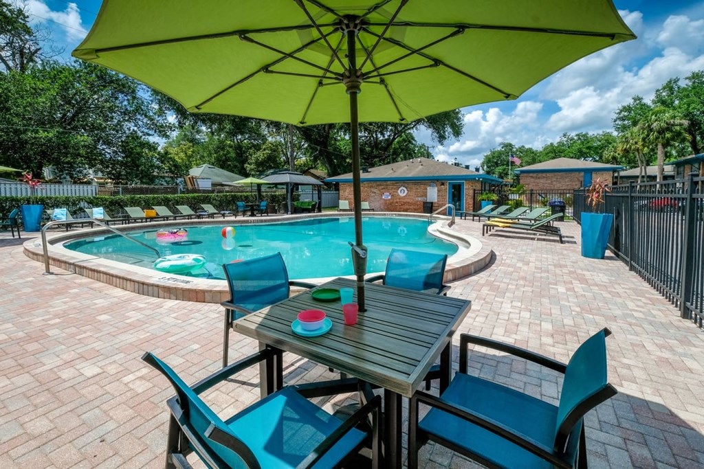 Poolside view of Community pool at Watermarc luxury Apartments in Lakeland, FL with patio table and chairs with large green umbrella.