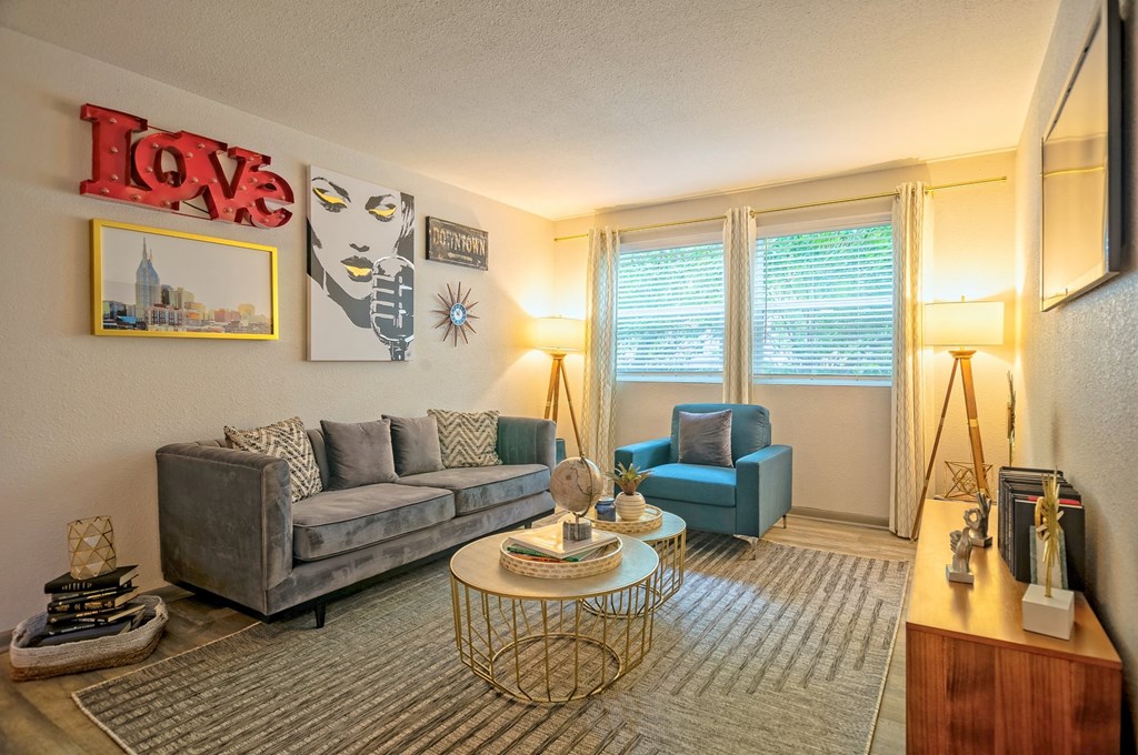 Living room in the Canvas Apartments in Nashville with large midcentury modern couch and sitting chair, large windows, and wood style flooring.