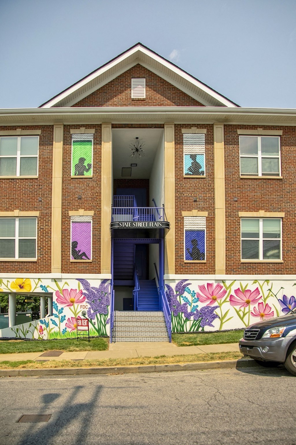 Front entrance of State Street Flats apartment building in west end of downtown Nashville. Large brick building has blue staircase and "for rent" sign.