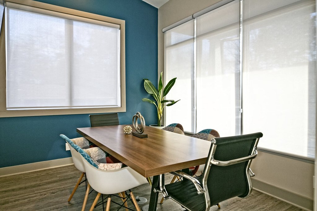 The Retreat at Indian Lake apartments lobby conference table with large windows with rolling blinds, six-chair table, and green palm in the corner.