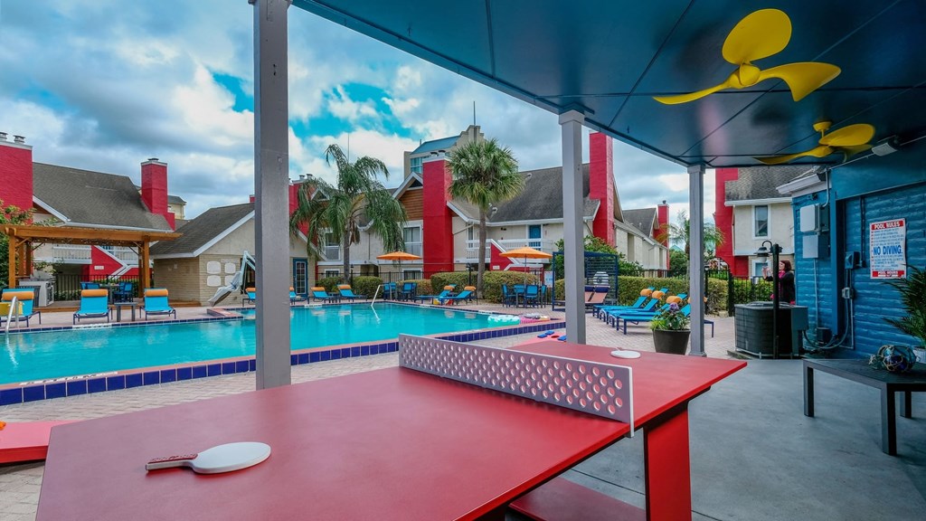 Fusion Orlando apartments community pool next to red ping pong table under awning with bright yellow ceiling fans.