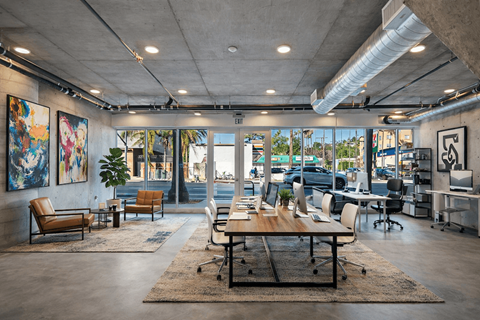 A modern office space with a large table and chairs in the foreground and a view of the outside through the windows at Fusion Hollywood.