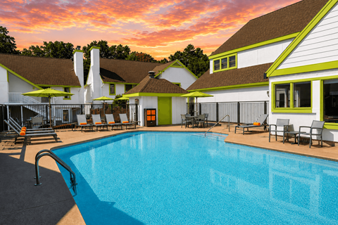 A swimming pool in front of a house with a sunset in the background.