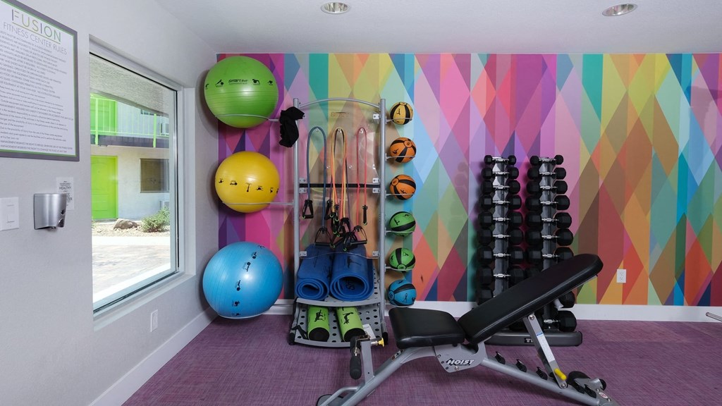 Fusion Las Vegas fitness center with weight training equipment and body weight equipment stored against a colorful geometric wall.