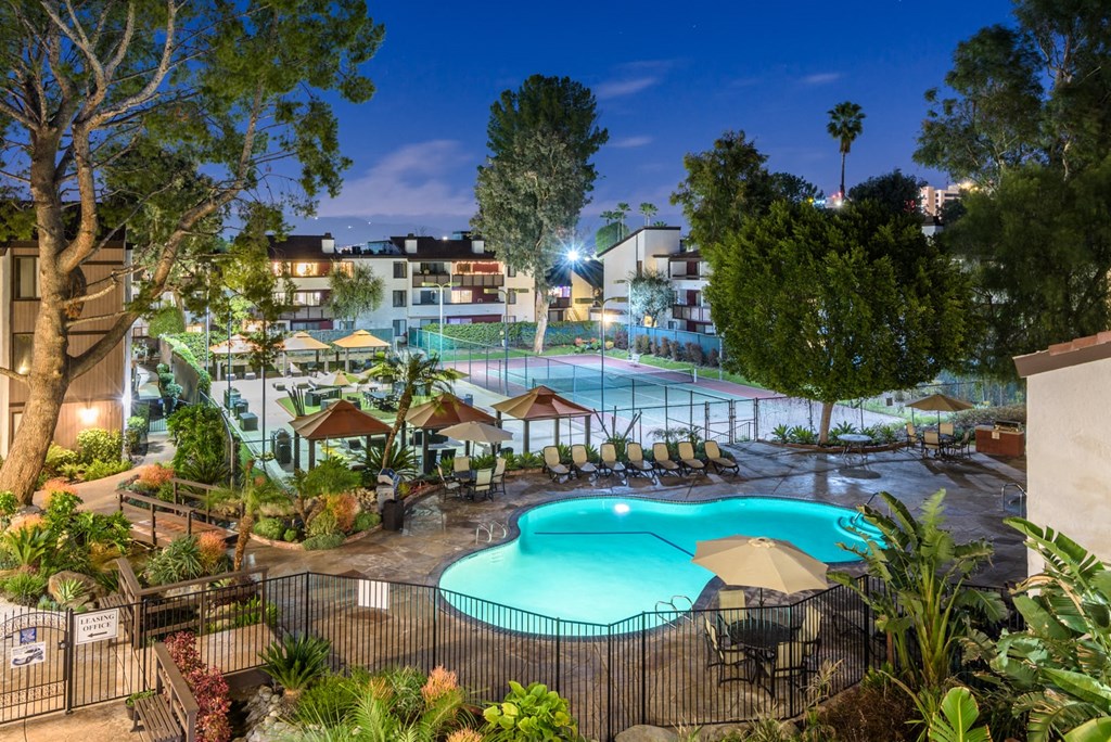 Fusion Warner Center apartments in Woodland Hills pool, courtyard, and tennis courts lit at night and surrounded by palm trees.