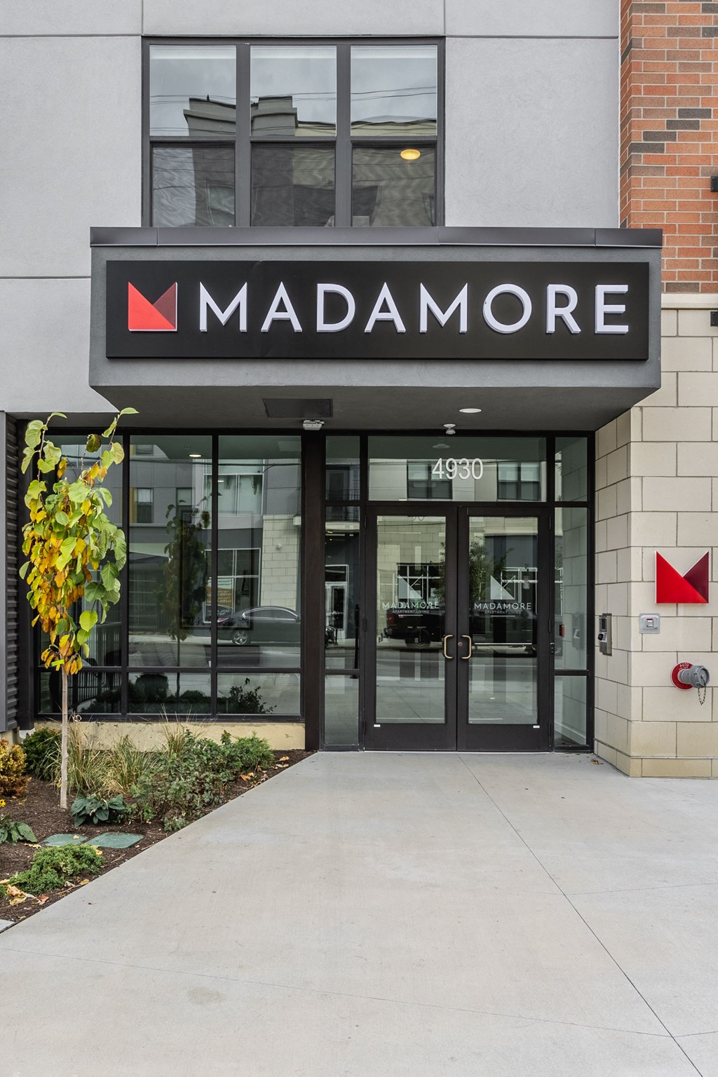 Front entrance of Madamore Apartments with a walkway and lush greenery.