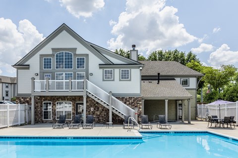 Swimming pool  surrounded by chairs and a white fence, in front of a clubhouse.