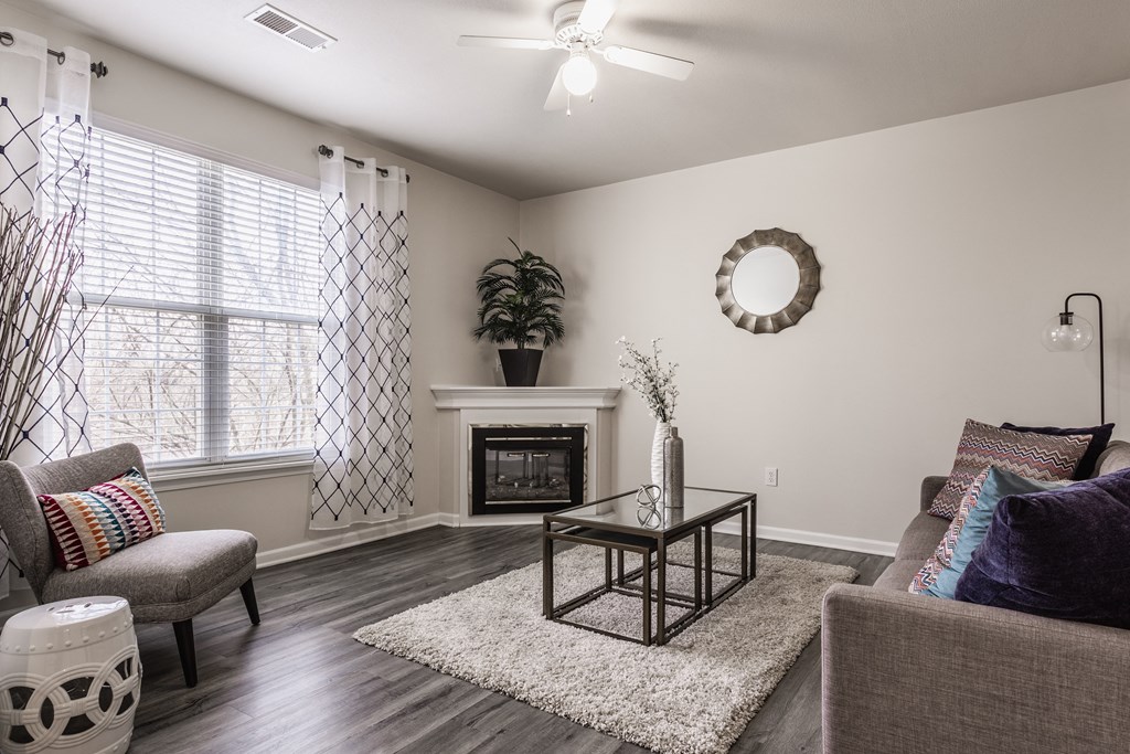 Eagle Creek, IN Apartments For Rent - Riverchase - Living Room With Hardwood Floors, A Ceiling Fan, A Decorative Fireplace, And A Window With Blinds