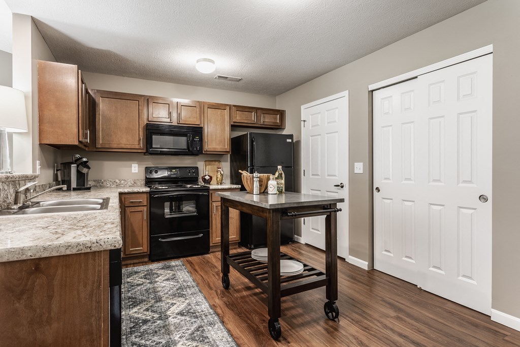 A kitchen with a kitchen island, black appliances, granite countertops, wooden cabinets, and hardwood-style flooring.