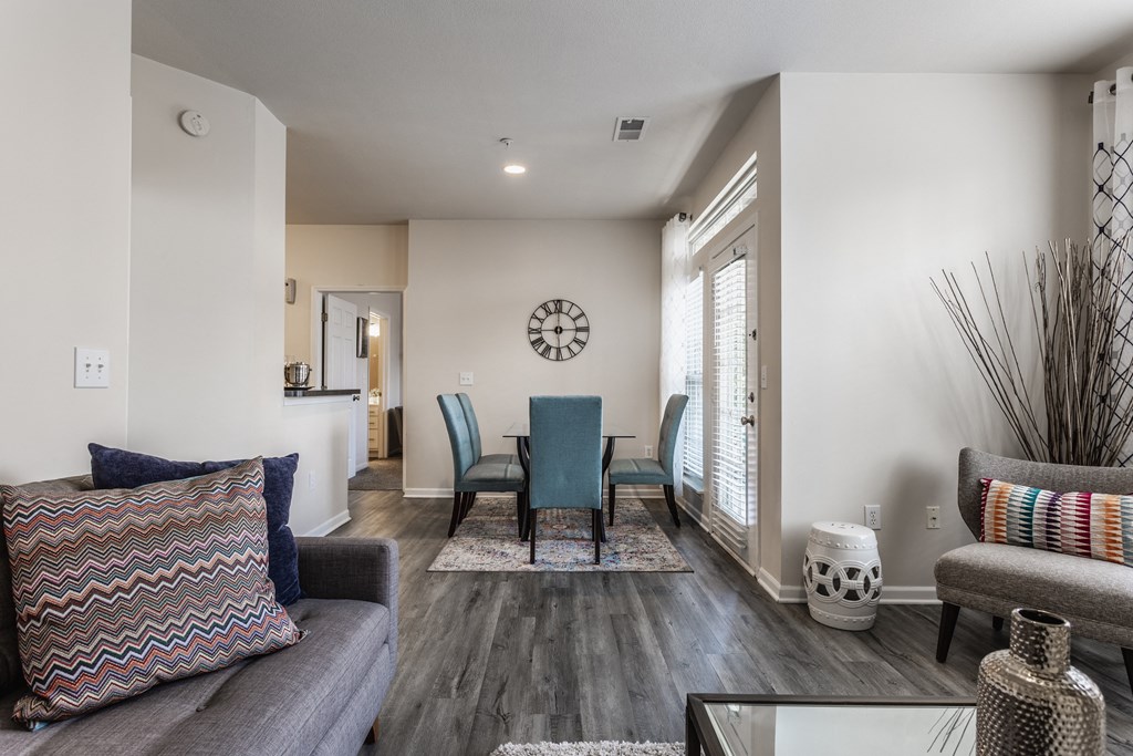 A living room with a couch and chair with decorative pillows, next to a dining room table, on hardwood-style floors.