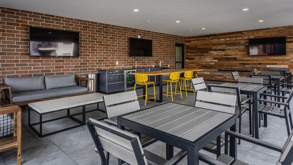 Sky lounge with outdoor furniture, tables and chairs, and three TV's.