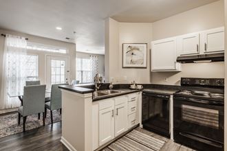 Clermont Apartments - Kitchen With Hardwood Floors, Black Appliances, And White Cabinets.
