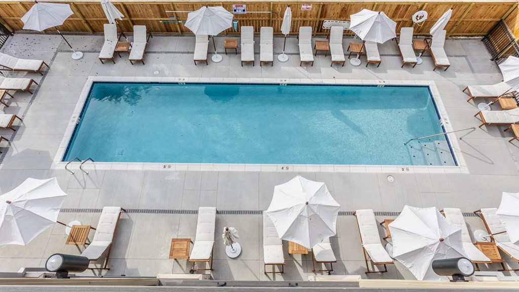 Aerial view of a swimming pool at Madamore with white chairs and umbrellas surrounded by a wooden fence.