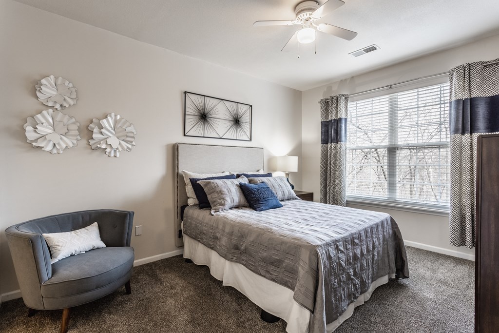 Eagle Creek, IN Apartments Near Downtown Indianapolis - Riverchase - Spacious Bedroom With Carpet Flooring, A Ceiling Fan, And A Window With Blinds