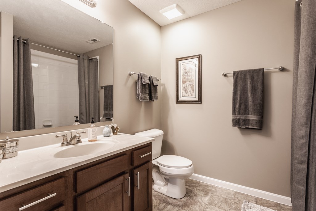 A beige bathroom with a vanity and a mirror, two hand towels, and tile flooring.