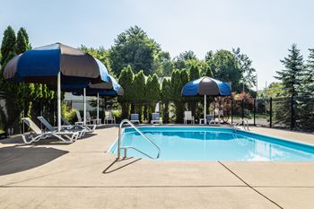 A swimming pool with a blue umbrella and lounge chairs.
