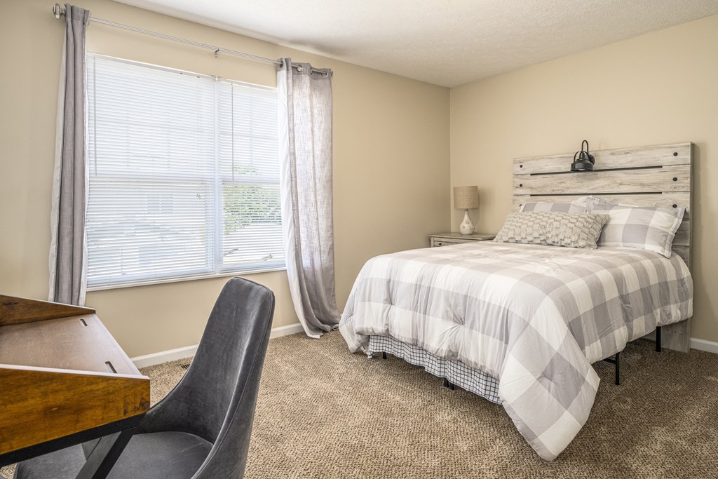 Three BR Apartments in Pickerington, OH - Arbors at Turnberry - Bedroom with Carpet Flooring, Bed, Nightstand, and a Desk with a Chair as well as a Window with Curtains