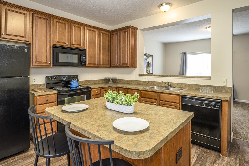 Pet Friendly Apartments in Pickerington, OH - Arbors at Turnberry - Kitchen with Wood-Style Cabinetry, Black Appliances, Granite-Style Counters, Overhead Lighting, as well as an Island with Seating