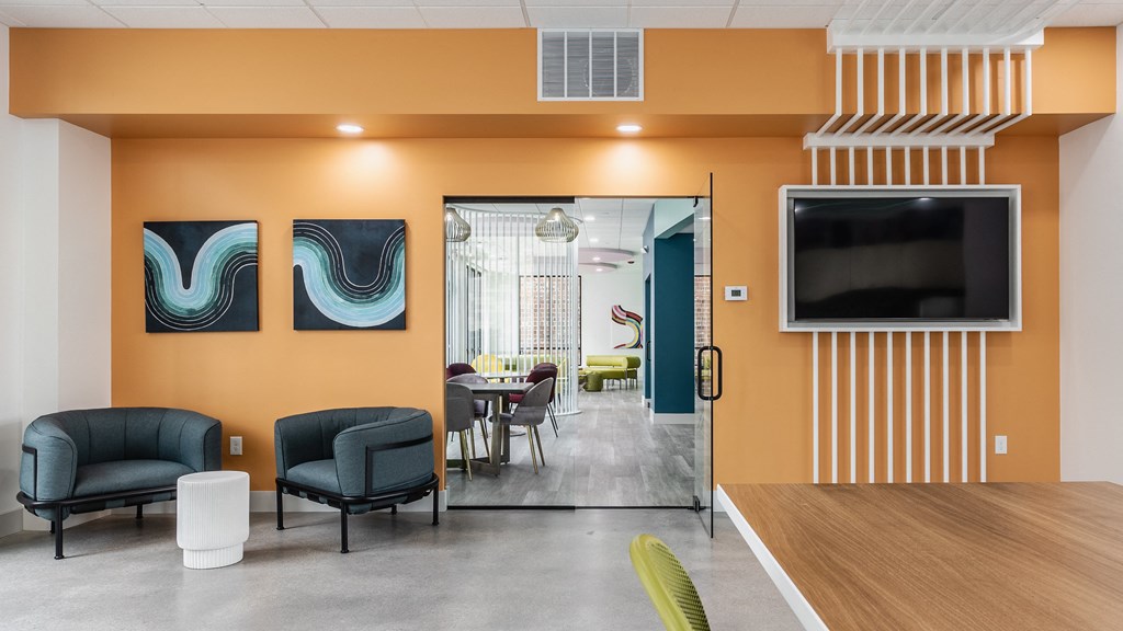 A lounge with two blue chairs, a TV, and a door leading to a seating area.