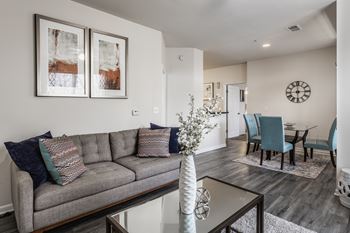 A living room with a grey couch and a white vase on a glass table.