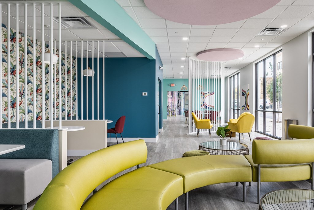 A green couch on hardwood-style floorings, next to tables and chairs in a co-working lounge.