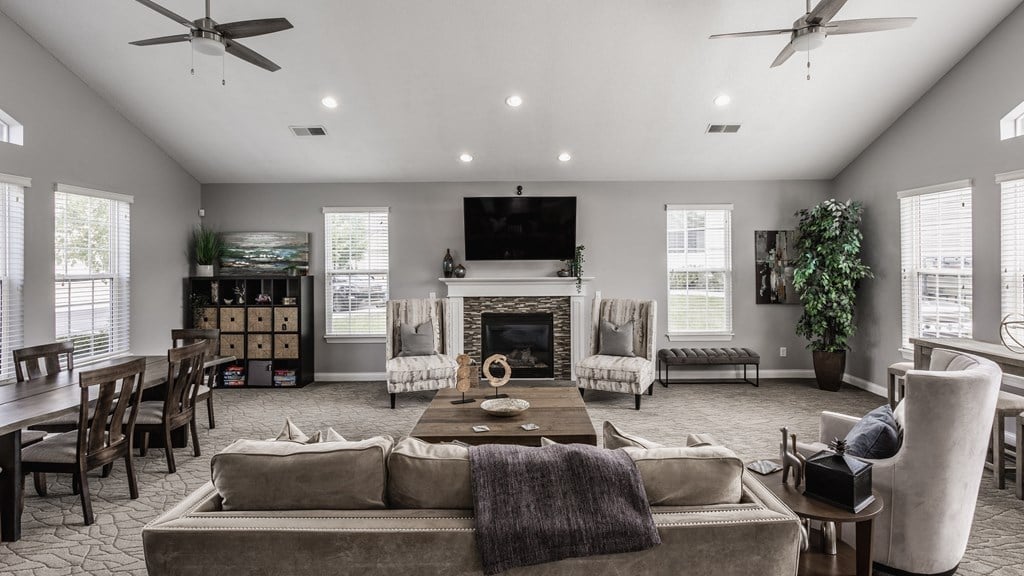 A spacious living room area with a couch, three chairs, a TV, a fireplace, windows, and carpeted flooring.