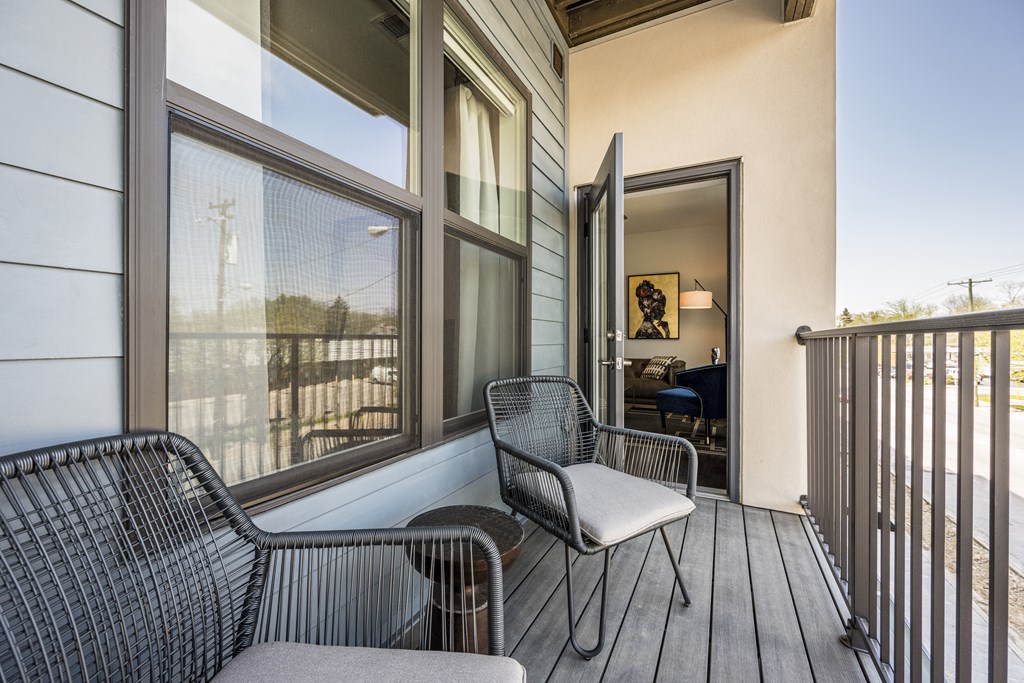 An apartment balcony with two chairs and a table in between, and a door leading to inside.