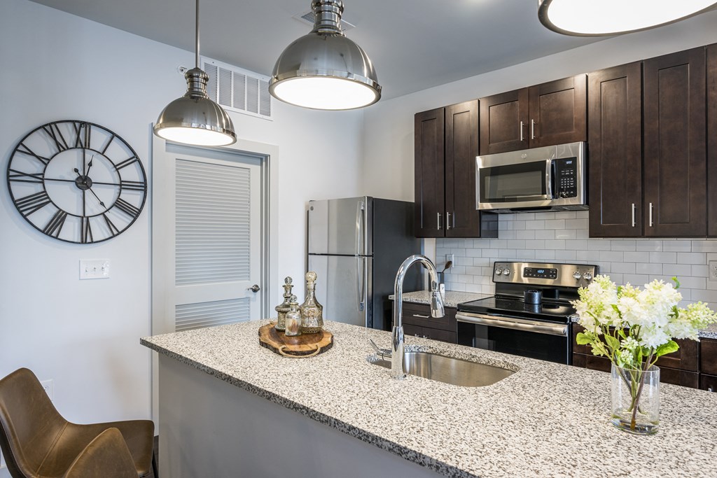A kitchen with dark cabinets, an island, and stainless steel appliances at Madamore Apartments.
