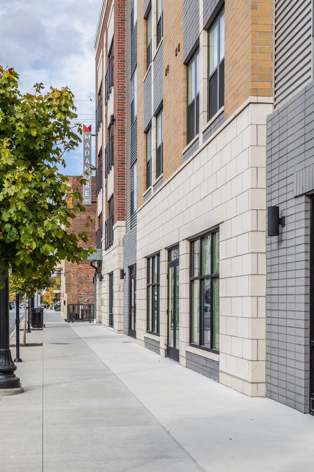 Madamore Apartments exterior with a sidewalk lined with trees.