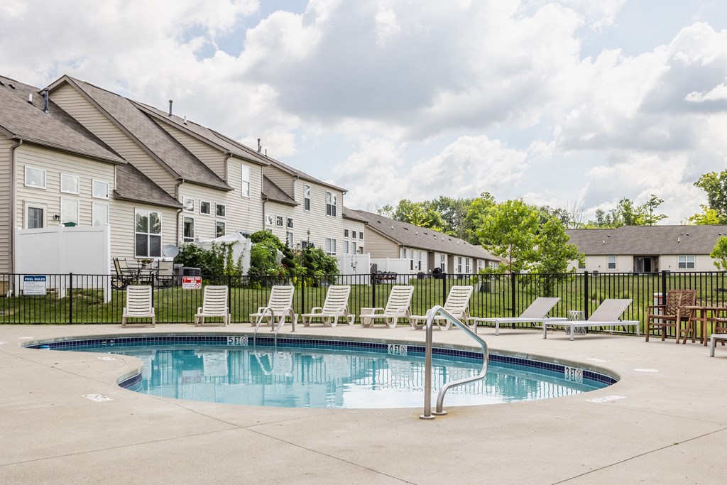 Swimming pool with white lounge chairs and a black fence, with apartment buildings in the background.