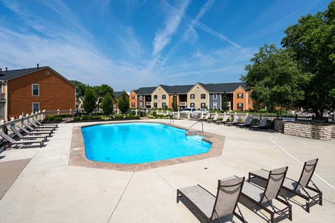 A swimming pool surrounded by lounge chairs and buildings in the background.