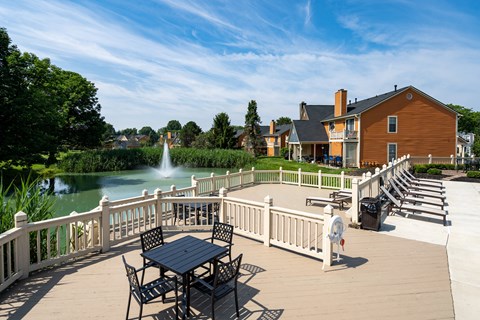 A patio with a table and chairs overlooks a pond and a house.