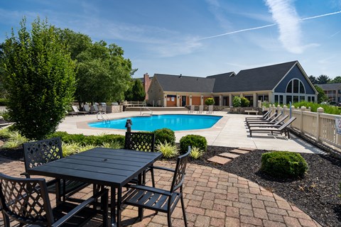A black table and chairs are set up outside in front of a house with a pool.