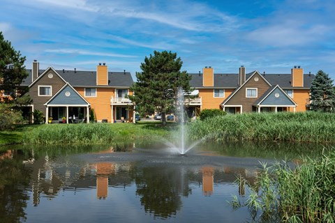 A fountain in the middle of a pond in front of a building.