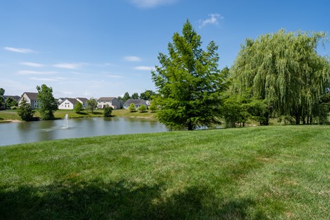 A serene landscape with a lake, houses, and trees.