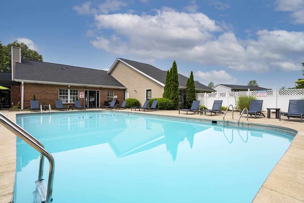 A large swimming pool in front of a building with a blue sky and clouds in the background.