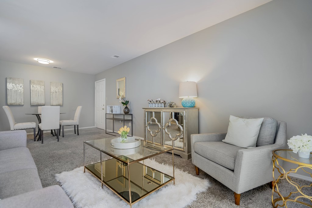 A modern living room with a glass coffee table and grey couches.