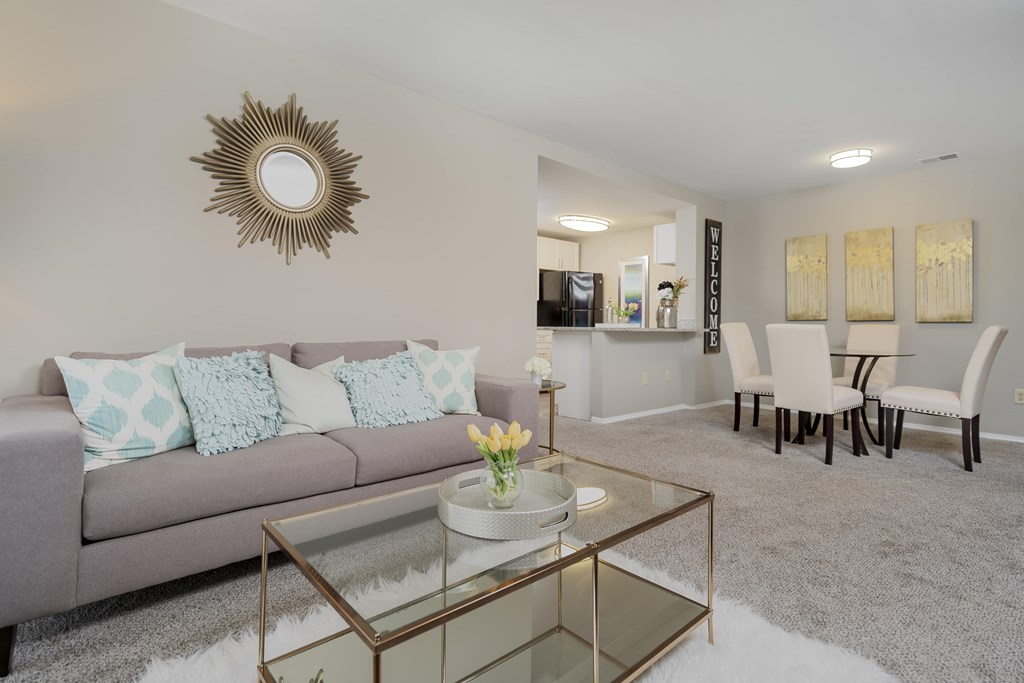 A living room with a grey couch, a glass coffee table, and a mirror on the wall.