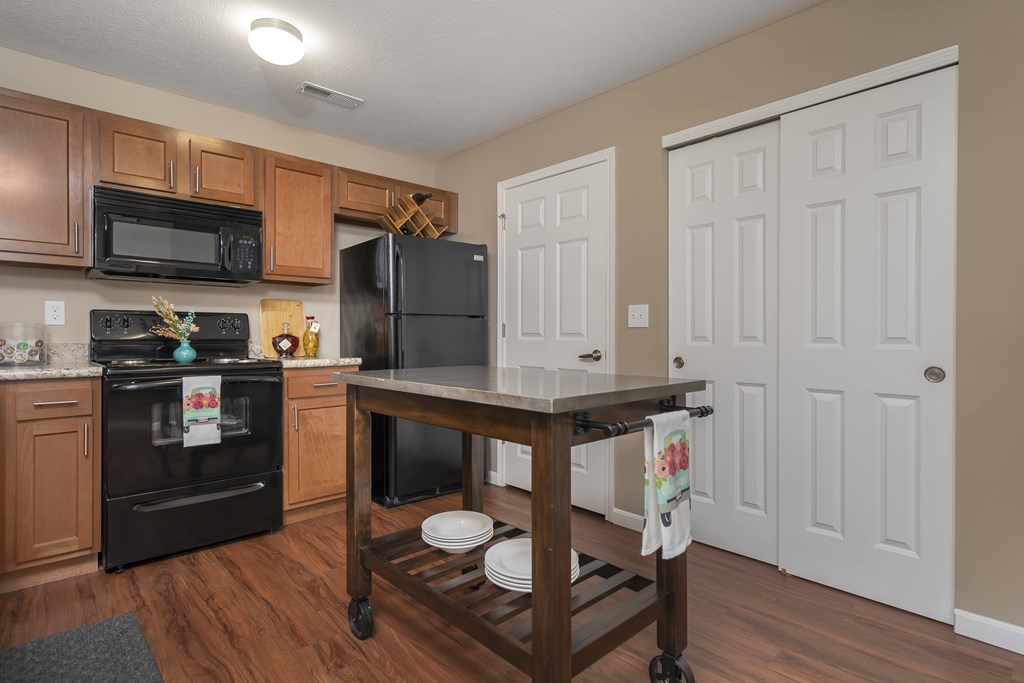 A kitchen with a black fridge and oven, wooden cabinets, and a wooden island with a towel hanging on it.