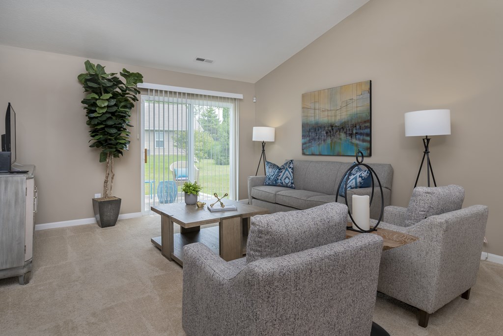 A living room with a grey couch, two chairs and a table with a vase on it.