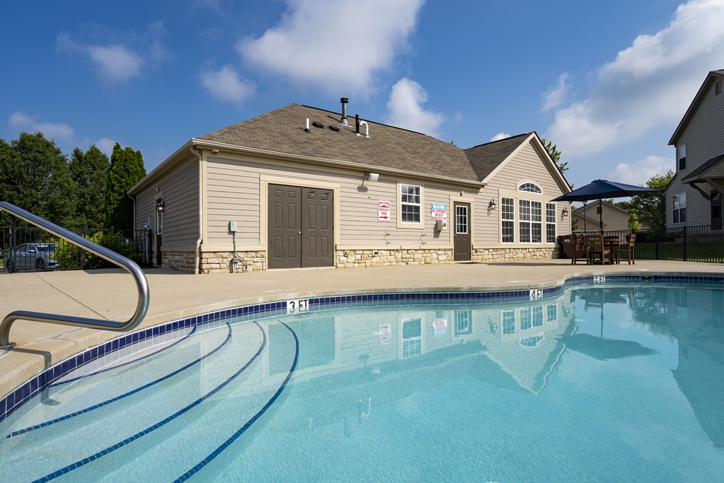 A swimming pool in front of a house with a slide.
