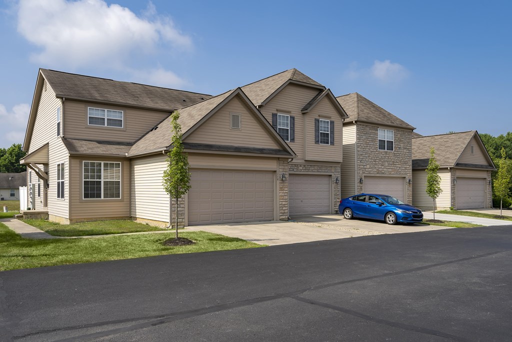 A blue car is parked in front of a house with a tree.