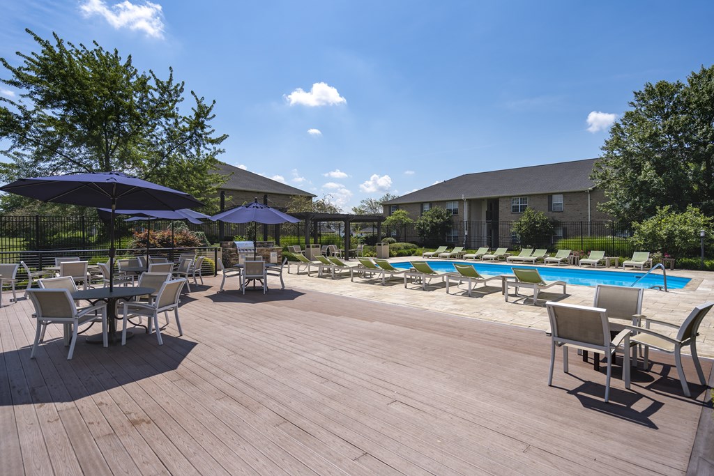 A wooden deck with chairs and umbrellas overlooking a pool.