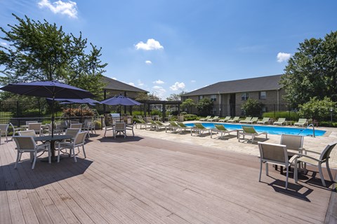 A wooden deck with chairs and umbrellas overlooking a pool.