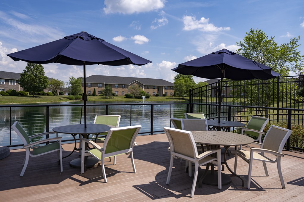 A table with chairs and umbrellas on a deck overlooking a lake.