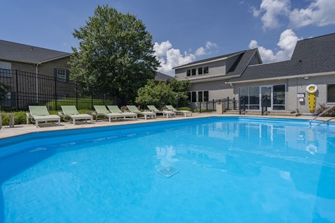 A large blue swimming pool with lounge chairs and a building in the background.